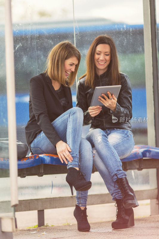 Two friends using digital tablet on bus station